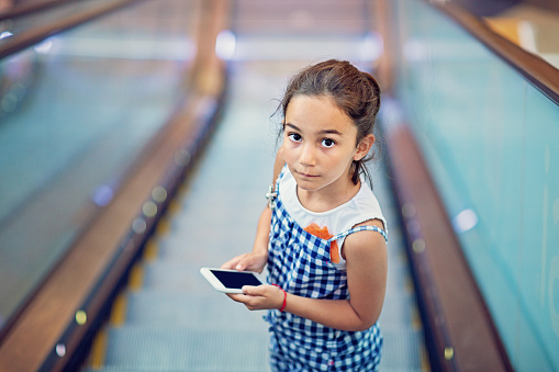 Sad little girl is texting on the escalator in the Mall