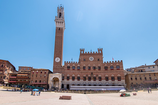 People walking in the Piazza del Campo in the morning of the Palio di Siena race at the city of Siena, in Tuscany, Italy. It is a shell shaped medieval public square and it is located in the historic center of Siena, an Unesco World Heritage site.