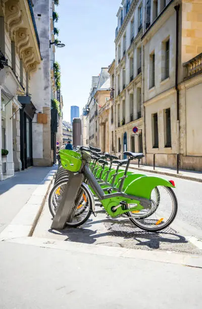 Photo of Green ecological electric bicycles with baskets for public rent await tourists cyclists on the streets of Paris