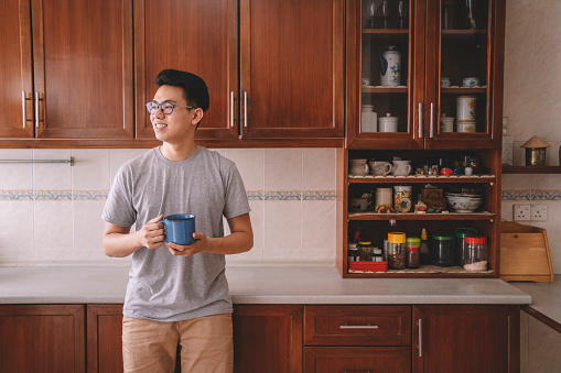 an asian chinese male having a cup of coffee in his kitchen in the morning before going to work