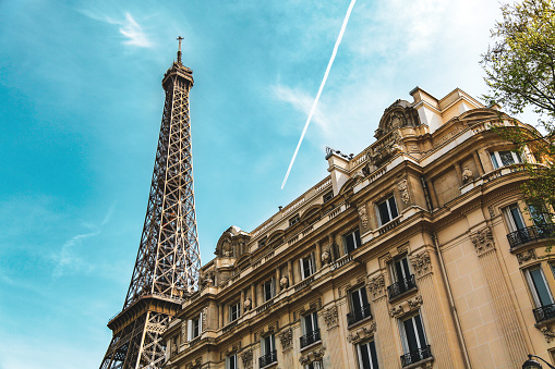 City street in Paris, France. Eiffel Tower and old french building in summer. Condensation trail of jet plane on blue sky.