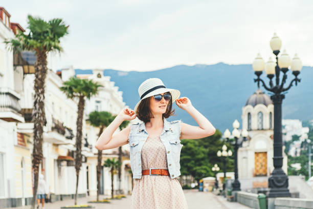 Beautiful woman in the street. Beautiful dark hair woman walking down the street along shops and palms, smiles and touches her straw hat. dark pink dress stock pictures, royalty-free photos & images