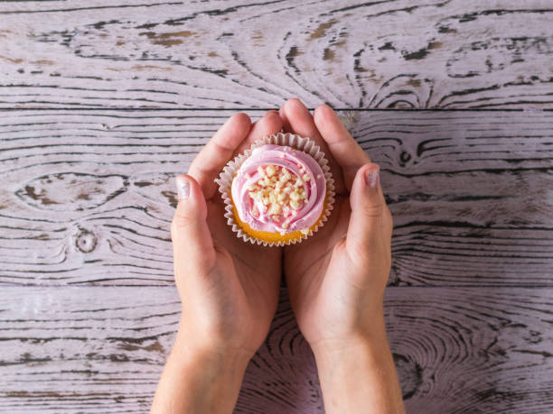 istock The child holds a fresh cupcake on a wooden table. 1160883833