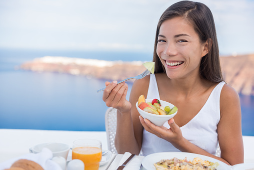 Healthy food. Beautiful woman eating bowl of fruit salad at breakfast at terrace. Young female is having healthy breakfast outdoor.