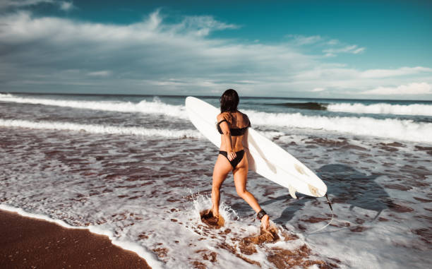 istock woman entering into the water with surfboard 1160904609