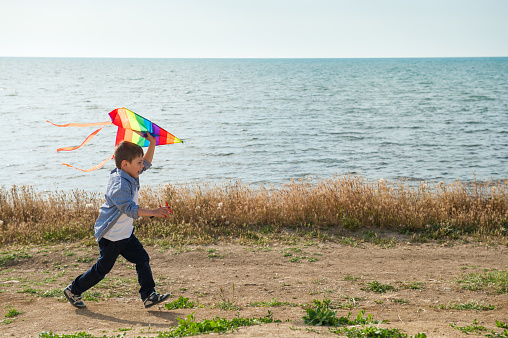 active happy kid running with colourful kite in his hands along sea shore