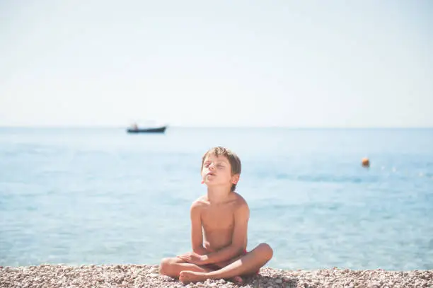 beautiful relaxing little kid sitting on summer sea beach with closed eyes dreaming during sunbathe yoga training