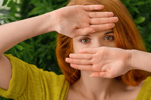 Beautiful redhead young woman hiding behind hands. Open palms flat towards camera.