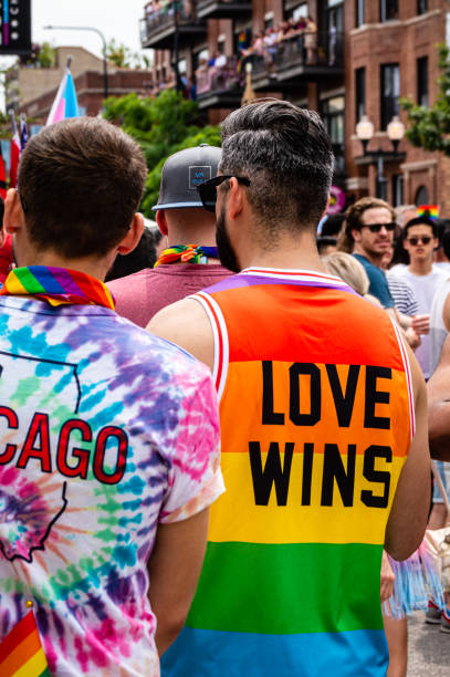 Man walking with friends at Gay Pride parade is wearing a rainbow colored shirt that reads "Love Wins" on the back side. stock photo