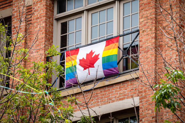 A gay pride rainbow flag with a Canada maple leaf is displayed in an apartment window. stock photo