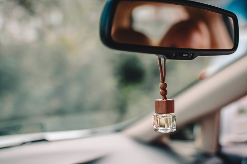 Car air perfume freshener inside the car with blurred green background. Little glass bottle with wooden lid and yellow aromatic liquid automobile freshener on car mirror.