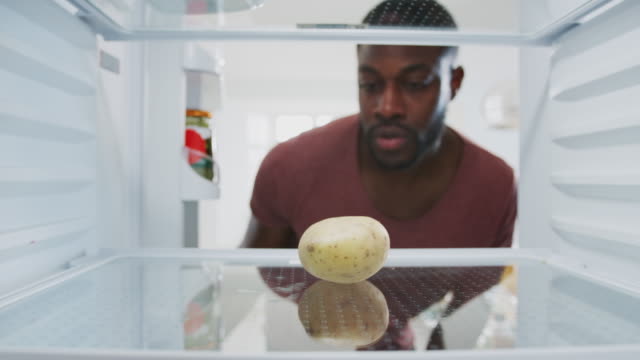 Disappointed Man Looking Inside Refrigerator Empty Except For Potato On Shelf