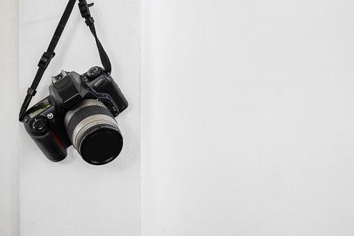 Old camera hanging on white concrete wall background