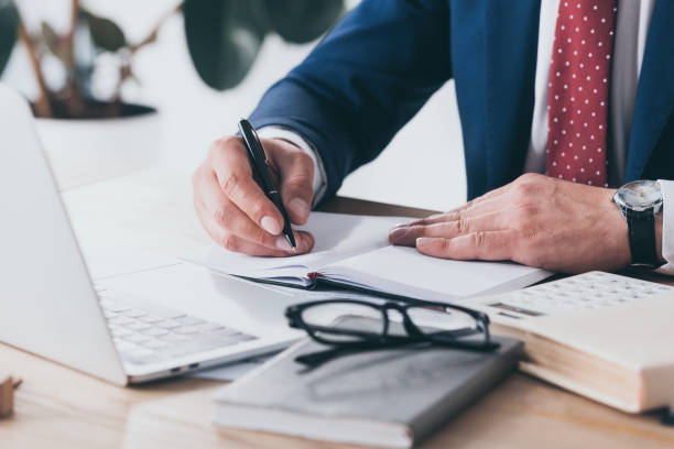 istock cropped view of manager in formal wear writing in notebook while sitting at workplace 1160924841