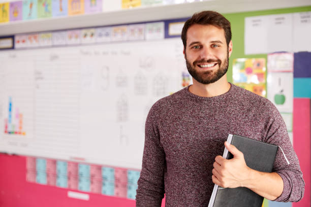 Portrait Of Male Elementary School Teacher Standing In Classroom Portrait Of Male Elementary School Teacher Standing In Classroom instructor stock pictures, royalty-free photos & images