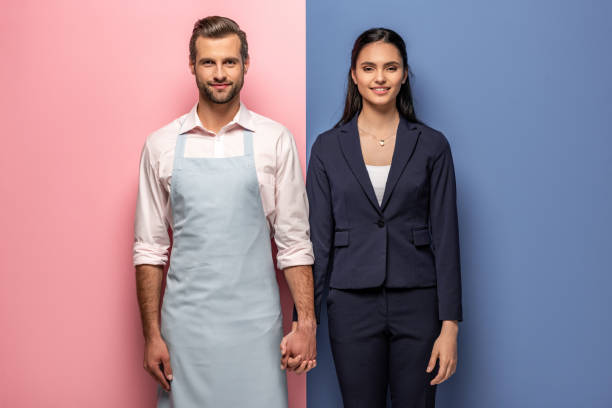 smiling man in apron and businesswoman holding hands on blue and pink smiling man in apron and businesswoman holding hands on blue and pink gender equality stock pictures, royalty-free photos & images