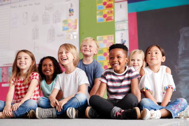 groupe d'élèves d'école primaire s'asseyant sur l'étage dans la salle de classe - élève photos et images de collection