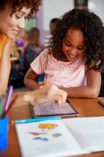 istock Elementary School Teacher And Female Pupil Drawing Using Digital Tablet In Classroom 1160927986