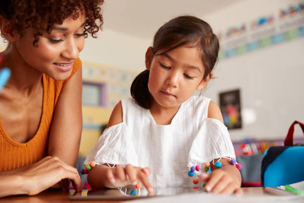 istock Elementary School Teacher And Female Pupil Drawing Using Digital Tablet In Classroom 1160927993