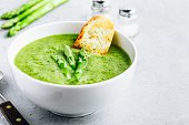 Asparagus cream soup with croutons on gray stone background.