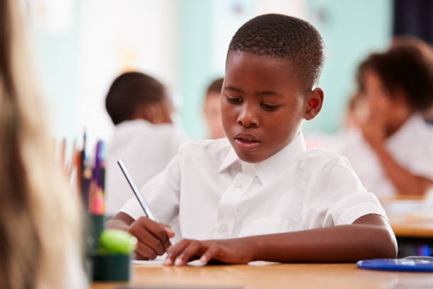 istock Male Elementary School Pupil Wearing Uniform Working At Desk 1160930181