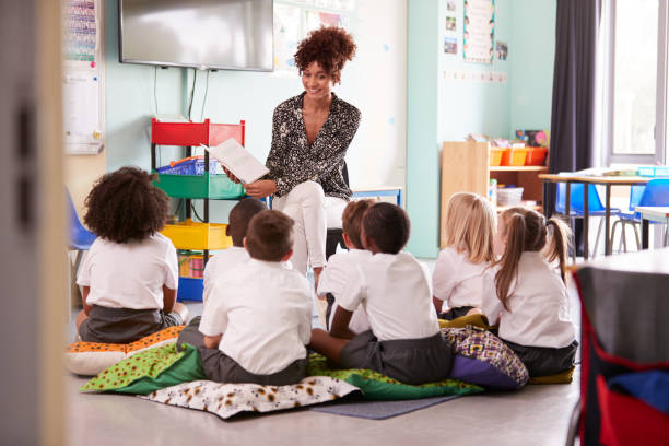 学校の教室で制服を着た小学生のグループに物語を読む女性教師 - elementary school elementary student education caucasian ストックフォトと画像