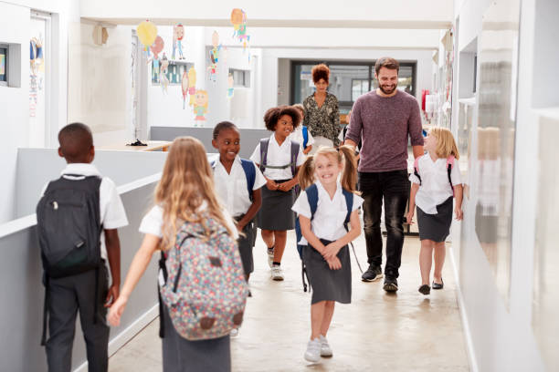 Teacher And Pupils Walking Along Corridor In Busy Elementary School Corridor Teacher And Pupils Walking Along Corridor In Busy Elementary School Corridor independent school education stock pictures, royalty-free photos & images