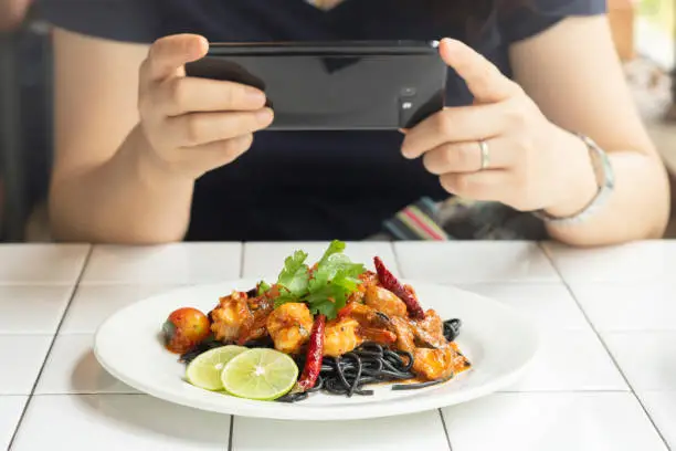 female take food photo with mobile phone spaghetti charcoal seafood on the table in restaurant