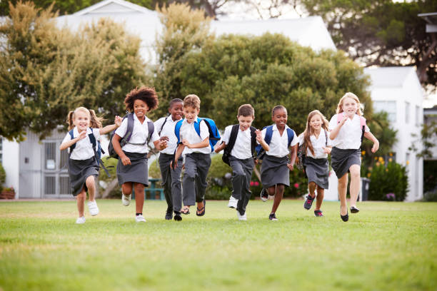 élèves excités d'école primaire utilisant l'uniforme courant à travers le champ au moment de pause - elementary student child student education photos et images de collection