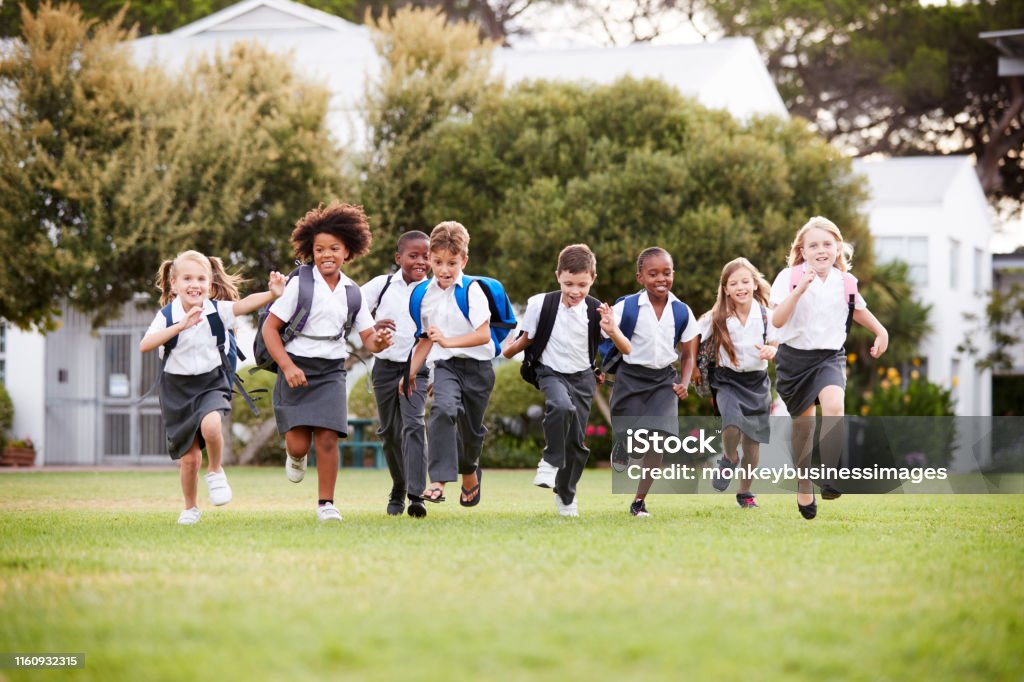 Excited Elementary School Pupils Wearing Uniform Running Across Field At Break Time Private School Education Stock Photo