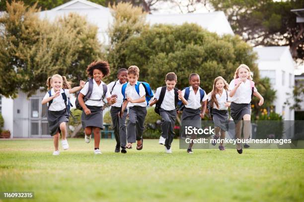 Excited Elementary School Pupils Wearing Uniform Running Across Field At Break Time Stock Photo - Download Image Now