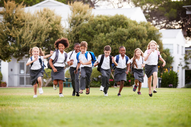 excited elementary school pupils wearing uniform running across field at break time - elementary student imagens e fotografias de stock