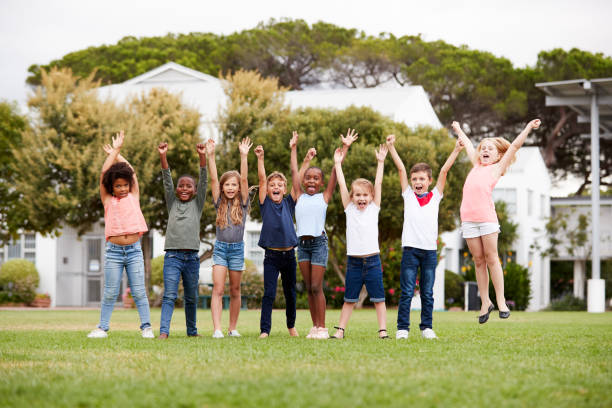 腕を上げて休憩時間に競技場に立つ興奮した小学生のグループ - elementary school elementary student education caucasian ストックフォトと画像