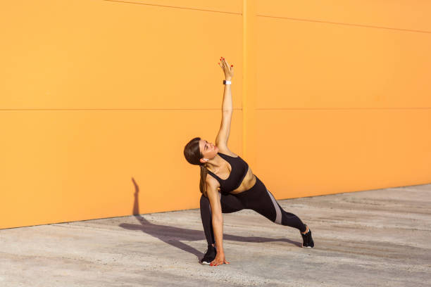 young beautiful yogi woman practicing yoga, doing utthita trikonasana exercise, extended triangle pose, working out, wearing sportswear black pants and top - one person child serene people failure imagens e fotografias de stock