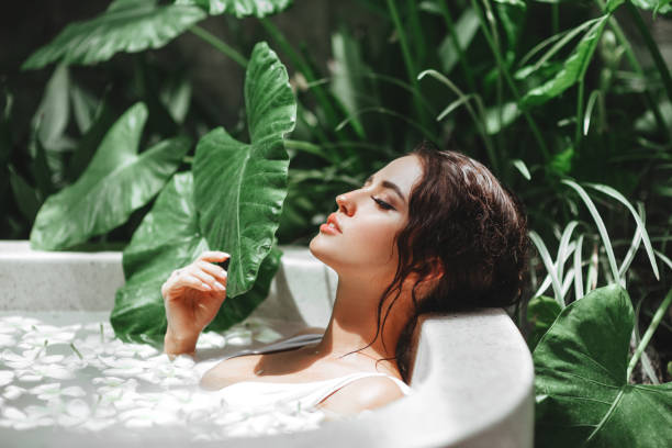 mulher que relaxa no banho ao ar livre redondo com flores tropicais. - bathtub women relaxation bathroom - fotografias e filmes do acervo