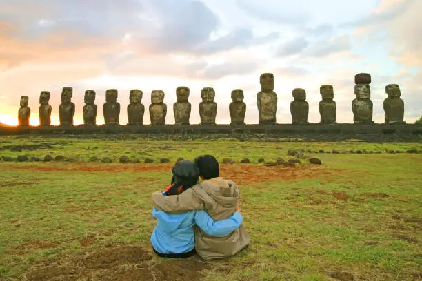 Photo of Couple having a happy moment in front of the awesome Moai statues of Ahu Tongariki at sunrise, Easter Island, Chile