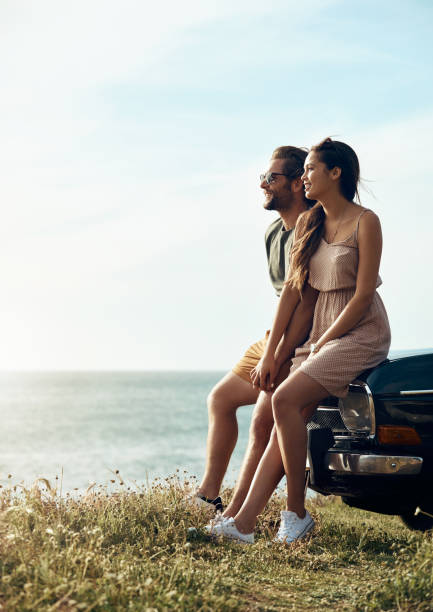 Picture perfect Full length shot of an affectionate young couple holding hands while sitting on a car by the ocean travel destinations 20s adult adventure stock pictures, royalty-free photos & images