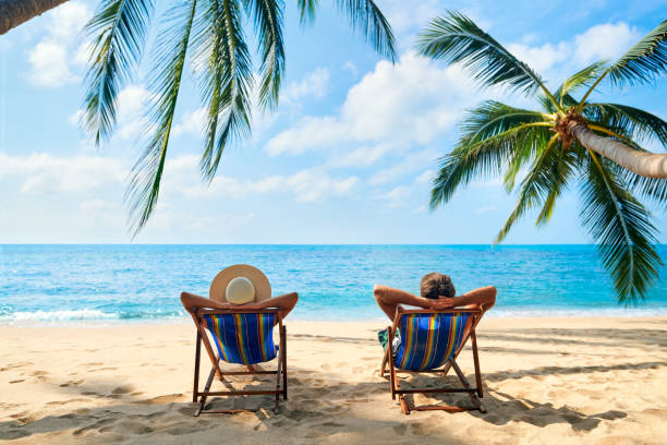 ビーチでリラックスしたカップルは、熱帯の島で美しい海を楽しみます - beach sun blue sky ストックフォトと画像