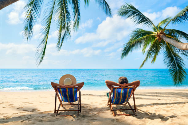 paar ontspannen op het strand genieten van prachtige zee op het tropische eiland - luxe fotos stockfoto's en -beelden