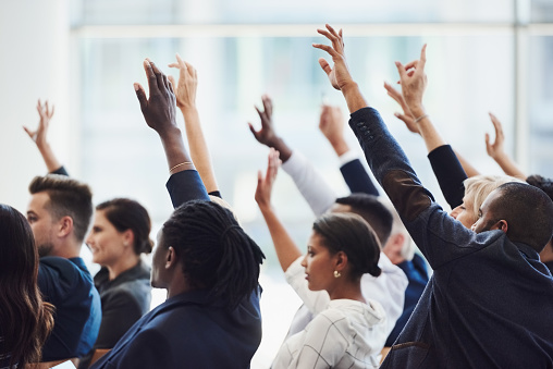 Shot of a group of businesspeople raising their hands to ask questions during a conference
