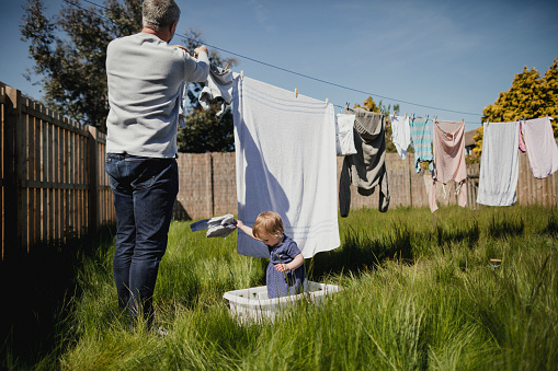 Mature father hanging out washing while caring for his baby daughter.