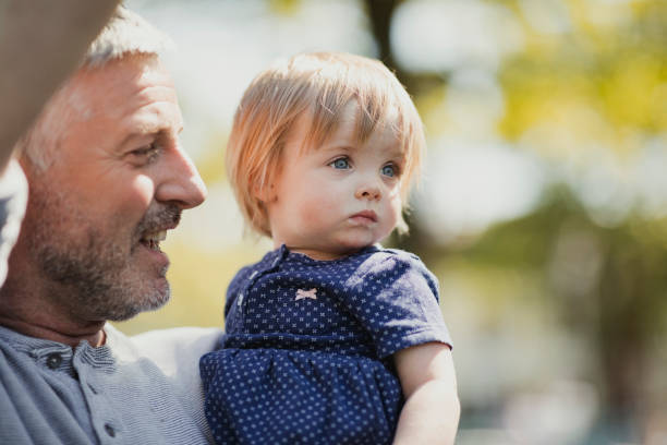 Close-up of a baby girl looking around while her father holds her outdoors.