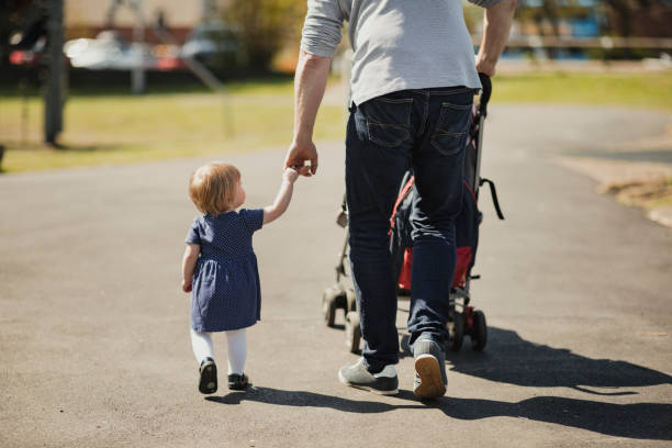 Strolling Through the Park Low angle view of a one year old girl holding her fathers hand as they walk through a public park. day in the life stock pictures, royalty-free photos & images