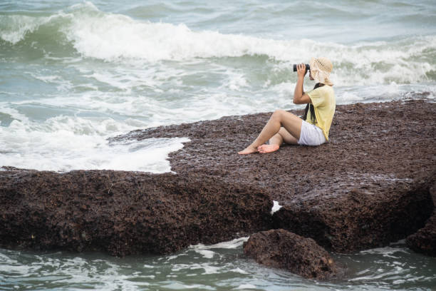 istock Asian pretty female sitting and resting on rocks and looking through Binoculars. 1160949290