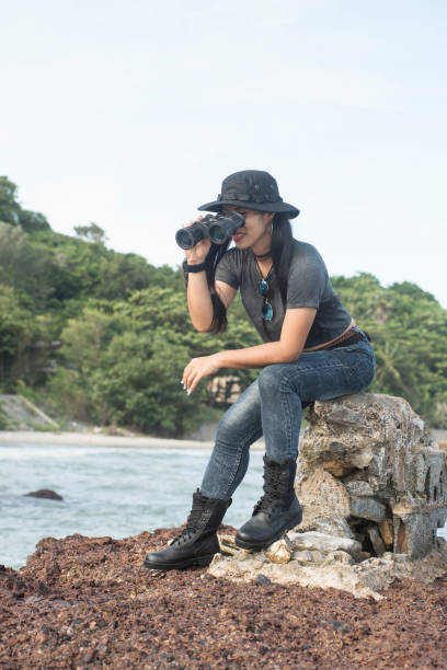istock Asian pretty female sitting and resting on rocks and looking through Binoculars. 1160949299