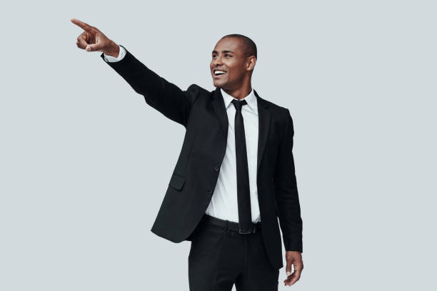 istock Look! Young African man in formalwear pointing somewhere and smiling while standing against grey background 1160963984