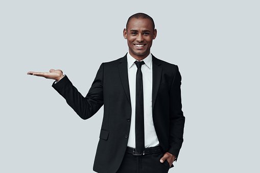 Take a quick look. Young African man in formalwear pointing copy space and smiling while standing against grey background