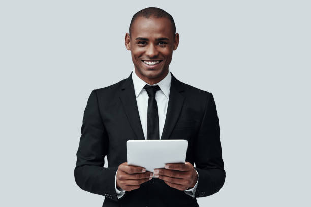 istock Business is his life. Charming young African man in formalwear working using digital tablet while standing against grey background 1160964845