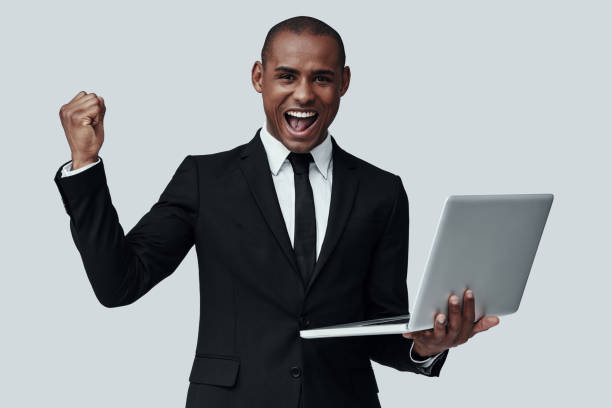 istock Success. Young African man in formalwear gesturing and smiling while standing against grey background 1160965136