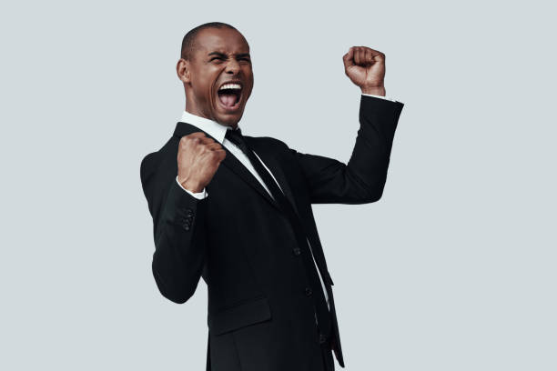 I did it! Handsome young African man in formalwear gesturing and shouting while standing against grey background